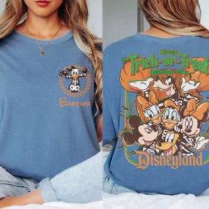 May include: A blue t-shirt featuring a small graphic of Donald Duck in a skeleton costume with the word Brother on the front. The back displays a large graphic of Mickey, Minnie, Donald, Daisy, and Goofy in skeleton costumes with the text Mickey's Trick-or-Treat Halloween Party and Disneyland.
