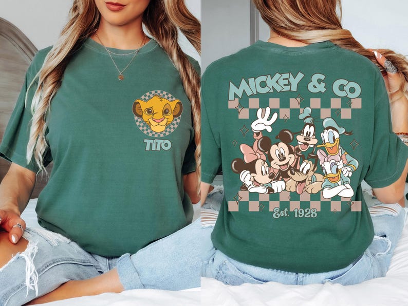 K&ouml;nnte beinhalten: Gr&uuml;nes T-Shirt mit einem Simba-Motiv und dem Namen "Tito". Auf der R&uuml;ckseite des Shirts befindet sich ein Mickey & Co.-Design mit Mickey, Minnie, Goofy, Donald und Daisy Duck. Der Text "Est. 1928" ist ebenfalls sichtbar.