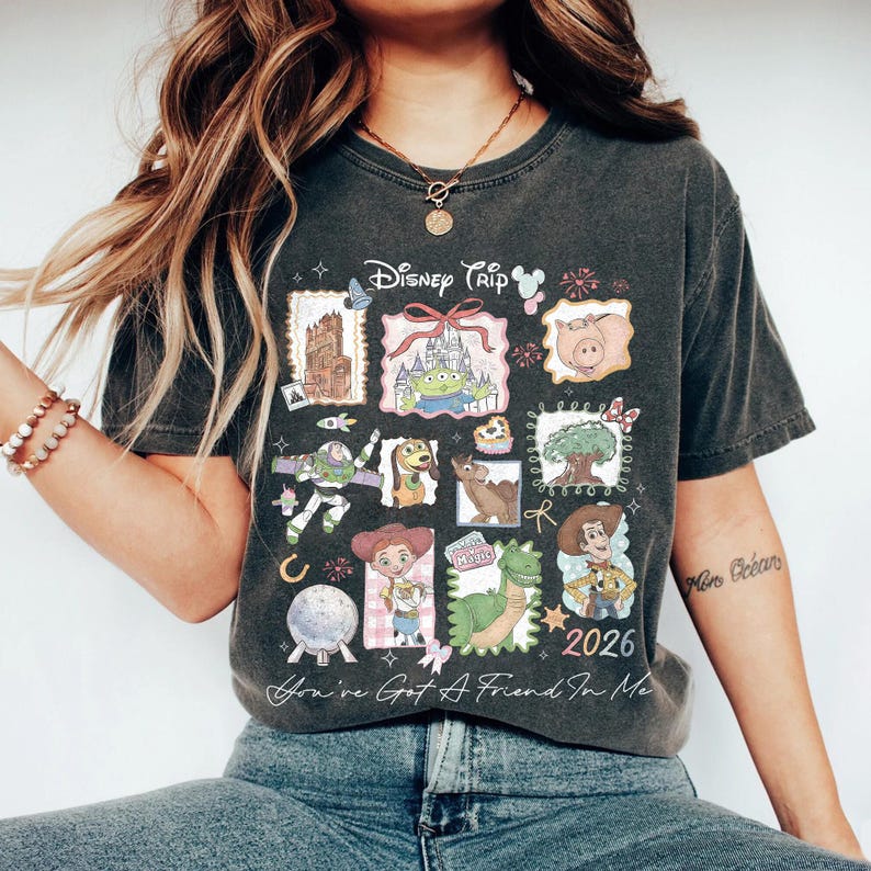 May include: Dark gray t-shirt featuring a collage of Disney characters and landmarks. The shirt includes the text "Disney Trip" and "2026", along with the phrase "You've Got A Friend In Me".