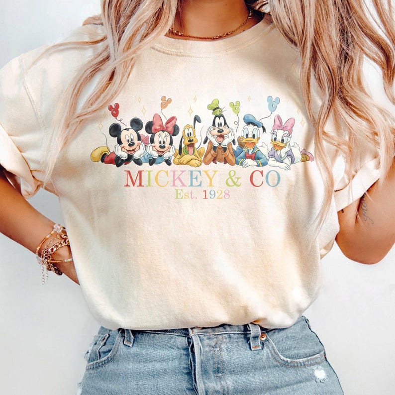 Puede incluir: Sudadera color crema con Mickey Mouse, Minnie Mouse, Pluto, Goofy, Donald Duck y Daisy Duck. El texto "Mickey & Co. Est. 1928" est&aacute; impreso debajo de los personajes en colores pastel. Cada personaje sostiene un globo.