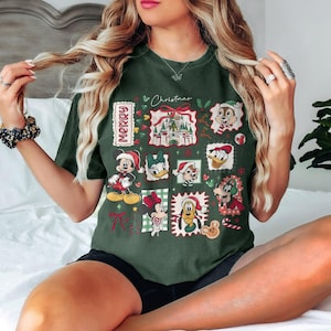 May include: Dark green t-shirt featuring a festive Christmas design with various Disney characters in holiday attire. The design includes Mickey Mouse, Minnie Mouse, Donald Duck, and others, along with the word "Merry".