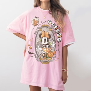 May include: Pink t-shirt featuring a Halloween-themed Minnie Mouse graphic. The design includes a skeleton Minnie, a pumpkin, and the words "Spotlight". The shirt has a double-layered look with white sleeves.