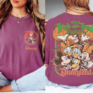 May include: A plum-colored t-shirt featuring a small circular graphic on the front with a skeleton-costumed character and the name Ashley. The back displays a large graphic of Disney characters in skeleton costumes with the text Mickey's Trick-or-Treat Halloween Party Disneyland.