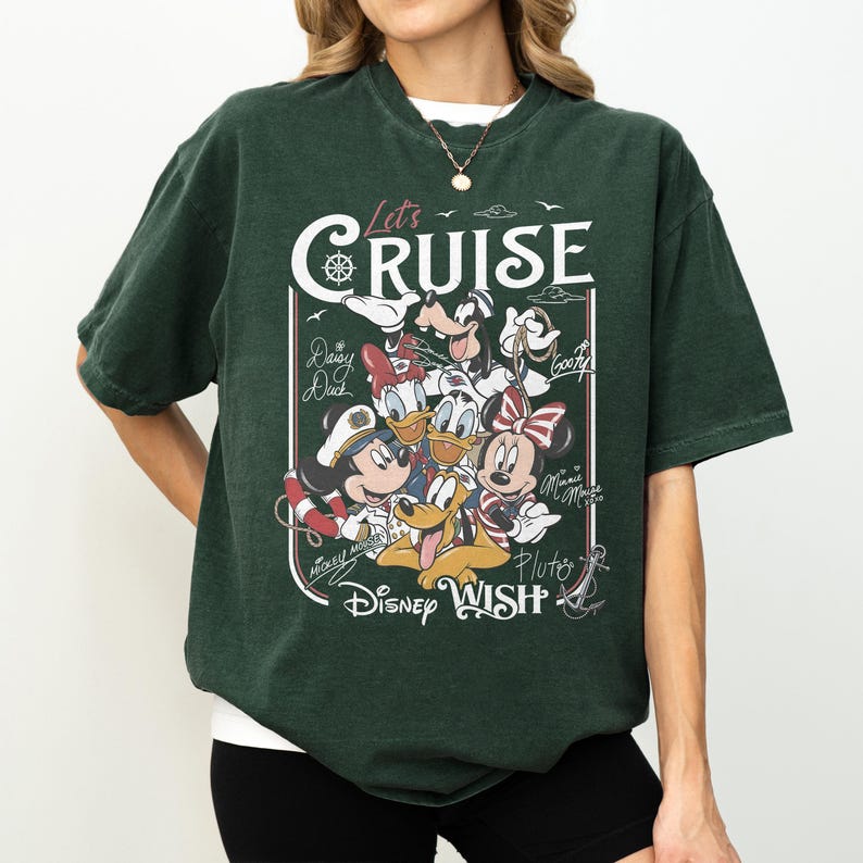 May include: Dark green t-shirt featuring a graphic of Disney characters, including Mickey Mouse, Minnie Mouse, Donald Duck, and Pluto. The shirt has the text "Let's Cruise" and "Disney Wish" in a white font.
