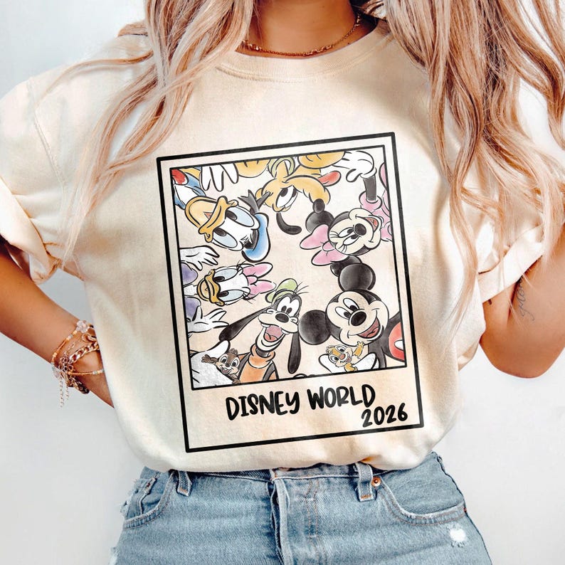 Puede incluir: Sudadera color crema con un gr&aacute;fico enmarcado de personajes de Disney, incluyendo Mickey Mouse, Donald Duck y Goofy. El gr&aacute;fico tiene las palabras "DISNEY WORLD 2026" en texto negro.