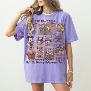 May include: A lilac-colored t-shirt featuring a graphic design with various Disney characters in Halloween costumes. The shirt includes the text "Walt Disney World" and "Mickey's Not-So-Scary Halloween Party 2026".