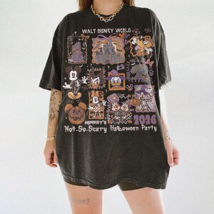 May include: Dark gray t-shirt featuring a graphic design with Disney characters in Halloween costumes. The shirt includes the text "Walt Disney World" and "Mickey's Not-So-Scary Halloween Party 2026". The design incorporates purple and orange accents.