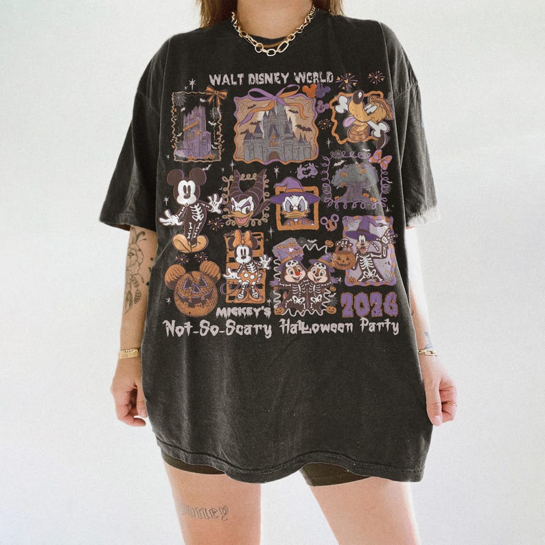May include: Dark gray t-shirt featuring a graphic design with Disney characters in Halloween costumes. The shirt includes the text "Walt Disney World" and "Mickey's Not-So-Scary Halloween Party 2026". The design incorporates purple and orange accents.