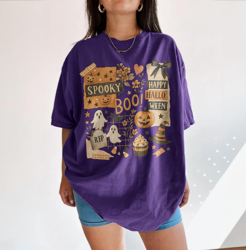 K&ouml;nnte beinhalten: Ein lila T-Shirt mit einem Halloween-Motiv. Das Design enth&auml;lt die W&ouml;rter "Spooky Boo! Happy Halloween" zusammen mit Bildern von Geistern, K&uuml;rbissen, einem Hexenhut und einem Cupcake.