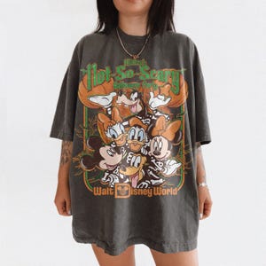 May include: A charcoal gray oversized t-shirt featuring a graphic print of Disney characters in skeleton costumes. The text reads Mickey's Not-So-Scary Halloween Party and Walt Disney World. The design includes orange pumpkins and green accents.