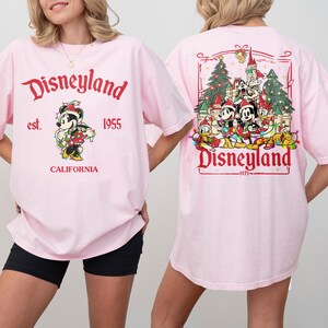 May include: Pink Disneyland t-shirts. The front features Mickey Mouse with text "Disneyland est. 1955 CALIFORNIA". The back has a Disneyland graphic with characters and text "Disneyland 1971".