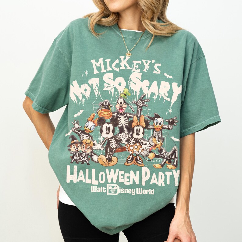 May include: Green t-shirt featuring a Halloween-themed graphic with Disney characters in skeleton costumes. The text on the shirt reads "Mickey's Not So Scary Halloween Party" and "Walt Disney World". The shirt has short sleeves and a crew neck.