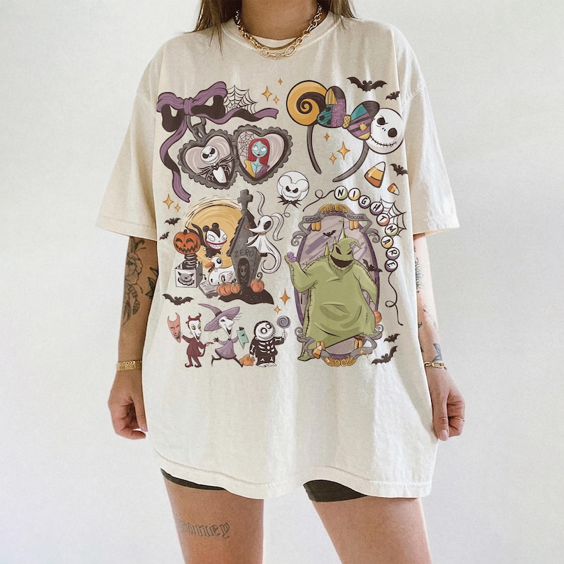 May include: Cream-coloured t-shirt featuring a colourful graphic design with characters and elements from "The Nightmare Before Christmas." The design includes Jack Skellington, Sally, Oogie Boogie, and other Halloween-themed imagery. The shirt has short sleeves and a relaxed fit.