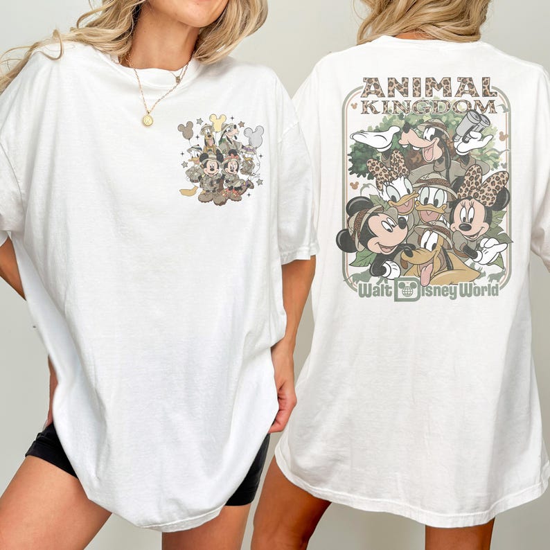Puede incluir: Camiseta blanca con dise&ntilde;os gr&aacute;ficos en la parte delantera y trasera. El dise&ntilde;o frontal incluye personajes de dibujos animados en camuflaje. El dise&ntilde;o trasero dice "ANIMAL KINGDOM" y "Walt Disney World" con personajes de dibujos animados con atuendo de safari.