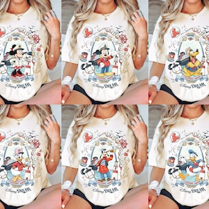 K&ouml;nnte beinhalten: Cremefarbene T-Shirts mit nautischen Disney-Charakter-Designs. Jedes Shirt zeigt einen anderen Charakter in einer gerahmten Illustration, mit dem Schriftzug "Disney Dream" unten. Zu den Charakteren geh&ouml;ren Micky, Minnie, Pluto, Donald, Daisy und Goofy.