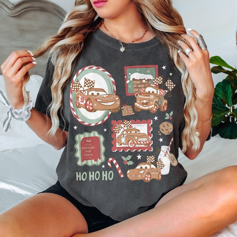 May include: Dark gray t-shirt featuring a festive design with gingerbread car illustrations, checkered flags, and holiday accents. The shirt includes the text "HO HO HO" and "Letters for Santa".