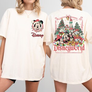 May include: Cream-colored t-shirt featuring Mickey Mouse in a Santa hat with the word "Daddy" below. The back of the shirt displays a Disneyworld graphic with various characters and the year 1971.