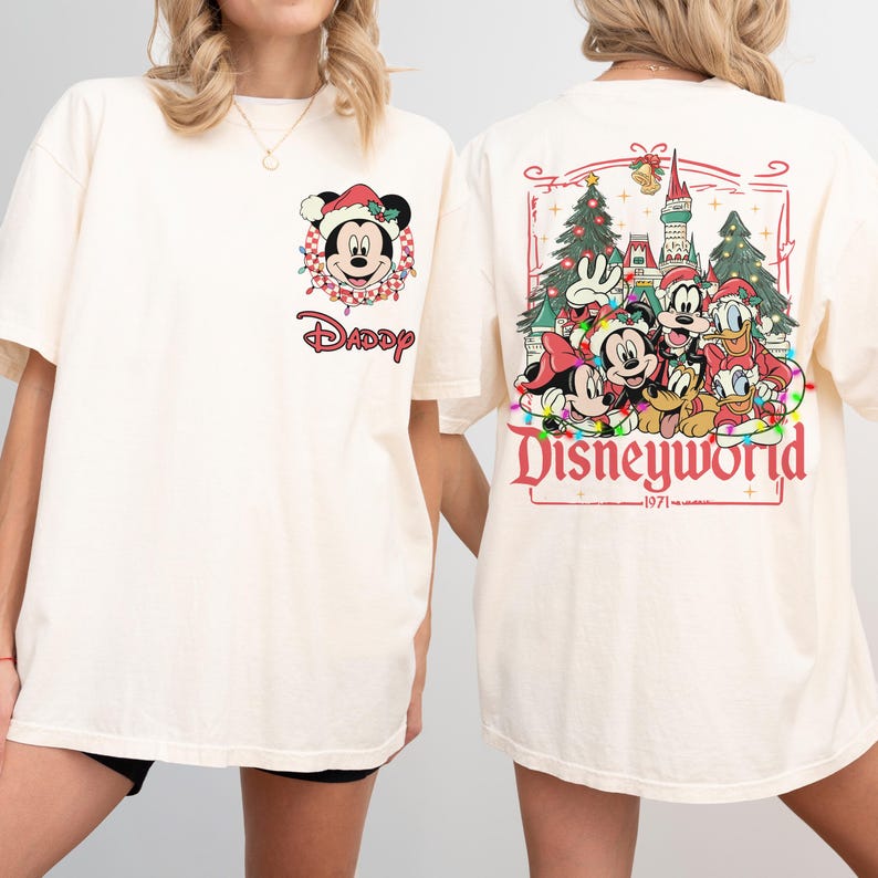 May include: Cream-colored t-shirt featuring Mickey Mouse in a Santa hat with the word "Daddy" below. The back of the shirt displays a Disneyworld graphic with various characters and the year 1971.