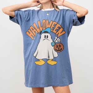 May include: Blue t-shirt with a Halloween graphic. The graphic features a cartoon ghost holding a jack-o'-lantern and wearing a hat. The word "Halloween" is printed above the ghost in orange letters.