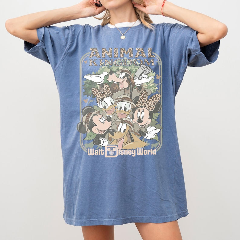 May include: Blue t-shirt featuring a graphic of Disney characters in safari attire, with the text "ANIMAL KINGDOM" and "Walt Disney World". The design includes Mickey Mouse, Minnie Mouse, Donald Duck, Goofy, and Pluto.