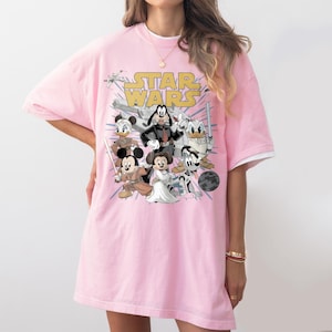 May include: Pink t-shirt featuring a graphic of Star Wars characters, including Mickey Mouse, Minnie Mouse, Donald Duck, and Goofy. The words "STAR WARS" are printed in yellow across the top of the design.