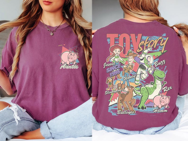 K&ouml;nnte beinhalten: Pflaumenfarbenes T-Shirt mit Toy Story-Motiv. Auf der Vorderseite befindet sich eine Schweinegrafik und das Wort "Auntie". Auf der R&uuml;ckseite sind das Toy Story-Logo und Charaktere wie Woody und Buzz Lightyear abgebildet.