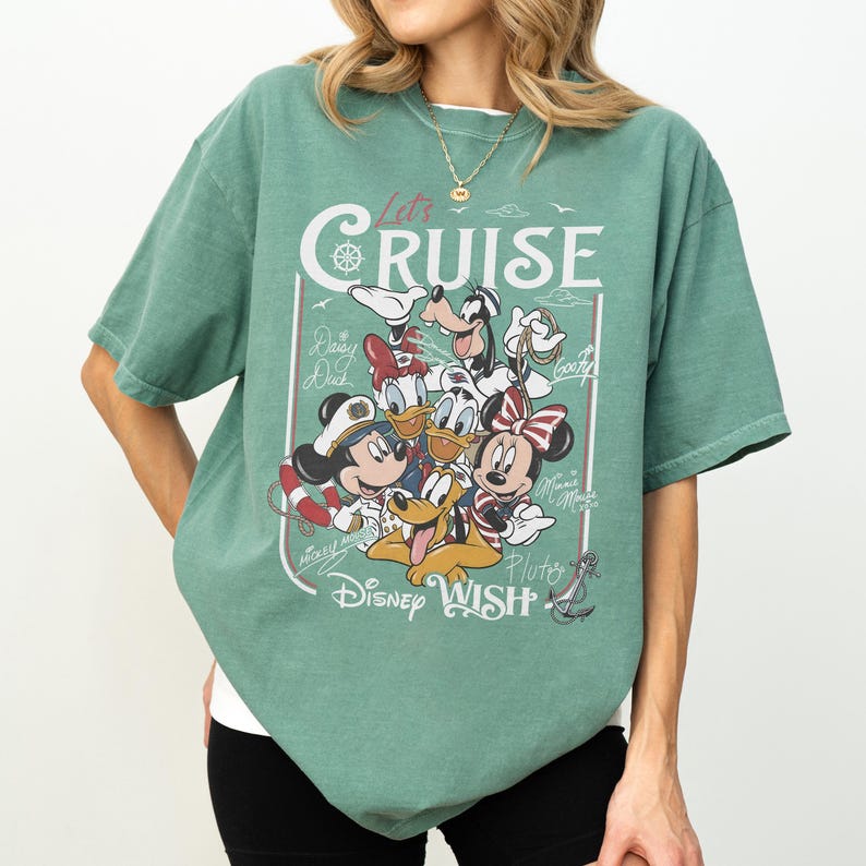 May include: Green t-shirt featuring a graphic of Mickey Mouse, Minnie Mouse, Donald Duck, Daisy Duck, Goofy, and Pluto. The text "Let's Cruise" and "Disney Wish" are also displayed on the shirt.