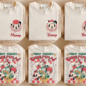 May include: Off-white t-shirts with Christmas-themed cartoon graphics. Designs include Minnie Mouse, Mickey Mouse, and Pluto in Santa hats, and the text "Mommy", "Daddy", and "Brother". Other shirts say "Very Merry Christmas".