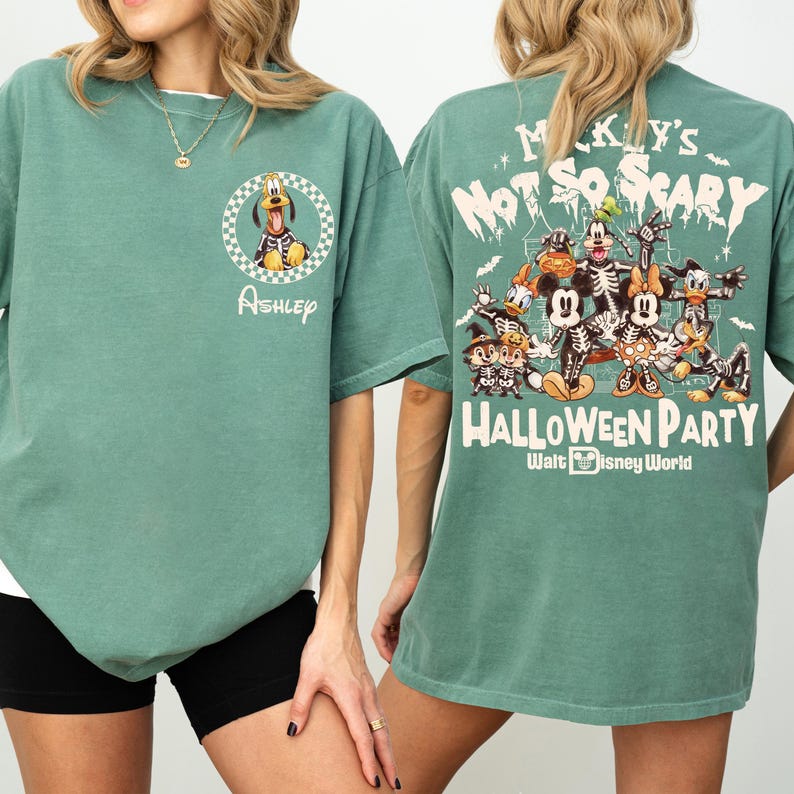 May include: A teal green t-shirt featuring a cartoon Pluto in a checkered circle and the name "Ashley". The back of the shirt displays a Halloween-themed graphic with Disney characters and the text "Mickey's Not So Scary Halloween Party".