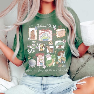 May include: Green t-shirt with a Disney Trip 2026 graphic featuring various cartoon characters. The shirt has a crew neck and short sleeves. The text "You've Got A Friend In Me" is printed at the bottom.