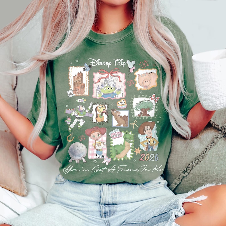 May include: Green t-shirt with a Disney Trip 2026 graphic featuring various cartoon characters. The shirt has a crew neck and short sleeves. The text "You've Got A Friend In Me" is printed at the bottom.