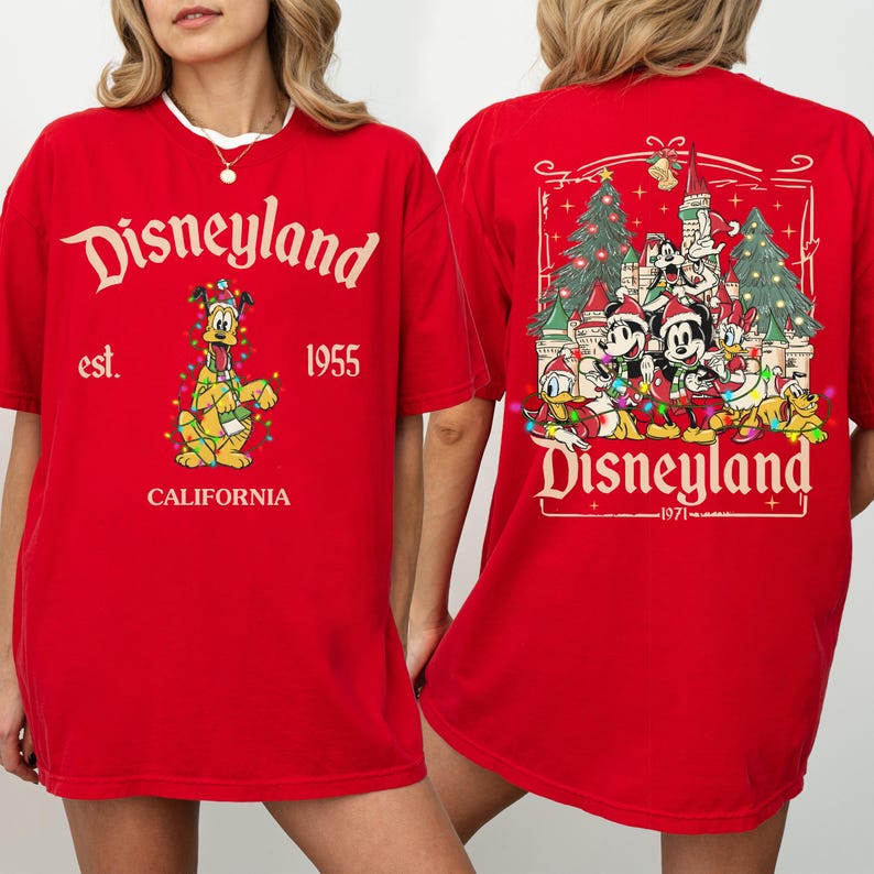 May include: Red Disneyland t-shirt with front and back graphics. The front features the Disneyland logo, Pluto, and the text "est. 1955 CALIFORNIA." The back displays Disney characters with Christmas decorations and the text "Disneyland 1971."