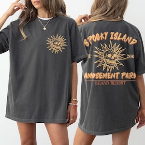May include: Dark gray t-shirt with a distressed skull and sunburst graphic on the front and back. The back of the shirt reads "Spooky Island Amusement Park Island Resort" in a vintage style.