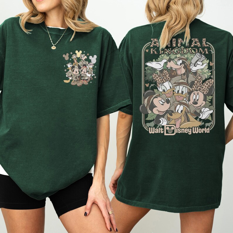Puede incluir: Camiseta verde oscuro con tem&aacute;tica de Disney. La parte delantera tiene un peque&ntilde;o gr&aacute;fico de Mickey Mouse y sus amigos. La parte trasera muestra un dise&ntilde;o m&aacute;s grande con el texto "Animal Kingdom" y "Walt Disney World" con varios personajes de Disney.