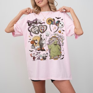 May include: A pale pink t-shirt with a vibrant graphic design featuring characters and elements from "The Nightmare Before Christmas." The design includes Jack Skellington, Sally, Oogie Boogie, and other iconic imagery. The shirt has a relaxed fit.