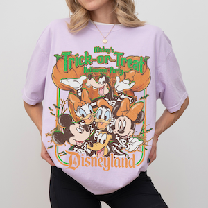 K&ouml;nnte beinhalten: Ein hellviolettes T-Shirt mit einem Grafikdruck von Mickey Maus, Minnie Maus, Donald Duck, Daisy Duck und Goofy in Skelettkost&uuml;men. Der Text lautet Mickey's Trick-or-Treat Halloween Party und Disneyland mit K&uuml;rbis-Akzenten.
