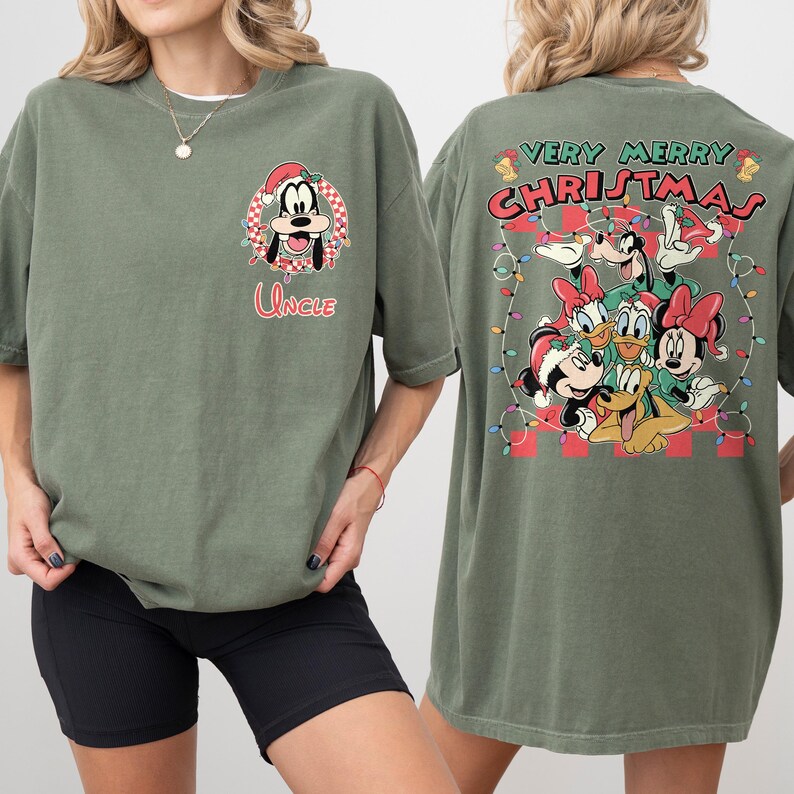 May include: Olive green t-shirt featuring a festive design. The front displays a cartoon of a dog wearing a Santa hat, with the word "Uncle" below. The back showcases a group of cartoon characters with the text "Very Merry Christmas".