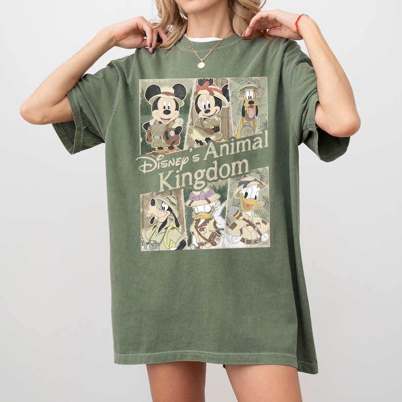 May include: Olive green t-shirt featuring a graphic of Disney's Animal Kingdom characters, including Mickey and Minnie Mouse, Goofy, Donald Duck, and Pluto. The design is in a vintage style, with the words "Disney's Animal Kingdom" printed on the front.