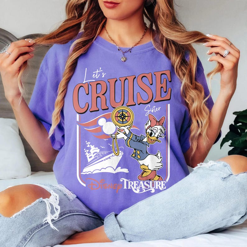 May include: A purple t-shirt with the words "Let's Cruise Sister" in a retro font. The graphic features Daisy Duck holding a compass, a cruise ship, and the words "Disney Treasure".