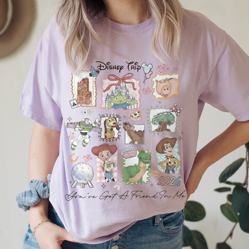 May include: A light purple t-shirt featuring a colorful graphic design with various Disney characters and the text "Disney Trip" and "2026". The shirt also includes the phrase "You've Got A Friend In Me".