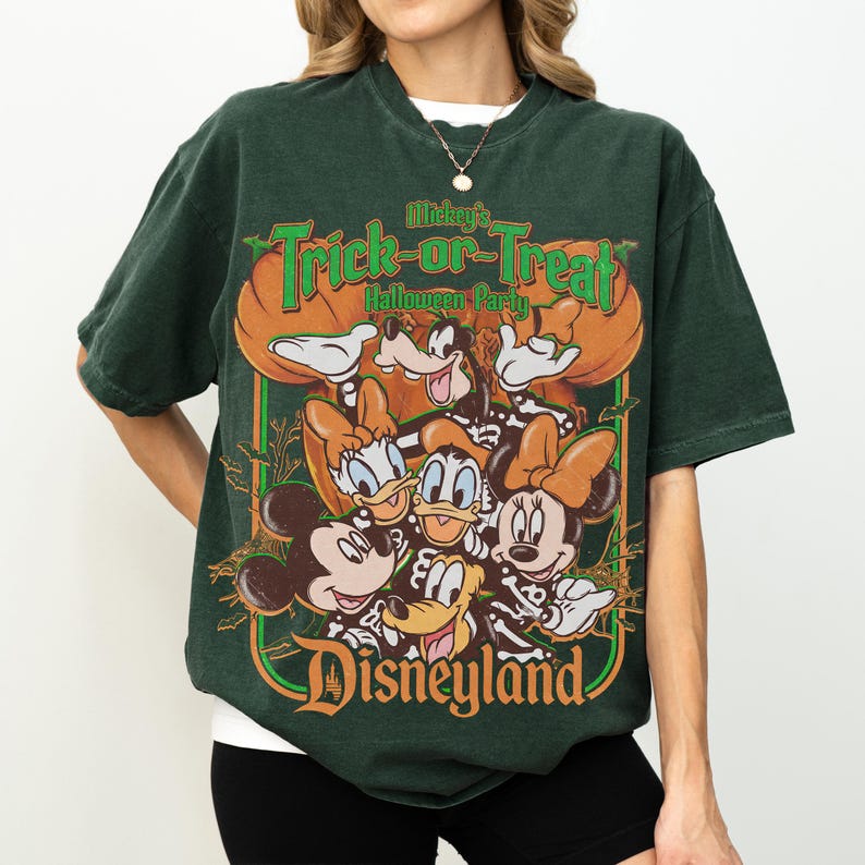 K&ouml;nnte beinhalten: Ein dunkelgr&uuml;nes Kurzarm-T-Shirt mit einem Grafikdruck von Mickey Mouse, Minnie Mouse, Donald Duck, Daisy Duck und Goofy in Skelettkost&uuml;men. Der Text lautet Mickey's Trick-or-Treat Halloween Party und Disneyland.