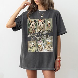 May include: Dark gray t-shirt featuring a graphic of Disney characters in safari outfits, including Mickey Mouse, Minnie Mouse, Pluto, Goofy, and Donald Duck. The text "Disney's Animal Kingdom" is printed below the characters.