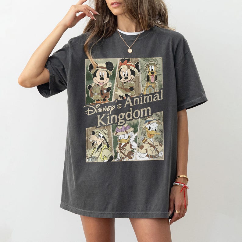 May include: Dark gray t-shirt featuring a graphic of Disney characters in safari outfits, including Mickey Mouse, Minnie Mouse, Pluto, Goofy, and Donald Duck. The text "Disney's Animal Kingdom" is printed below the characters.