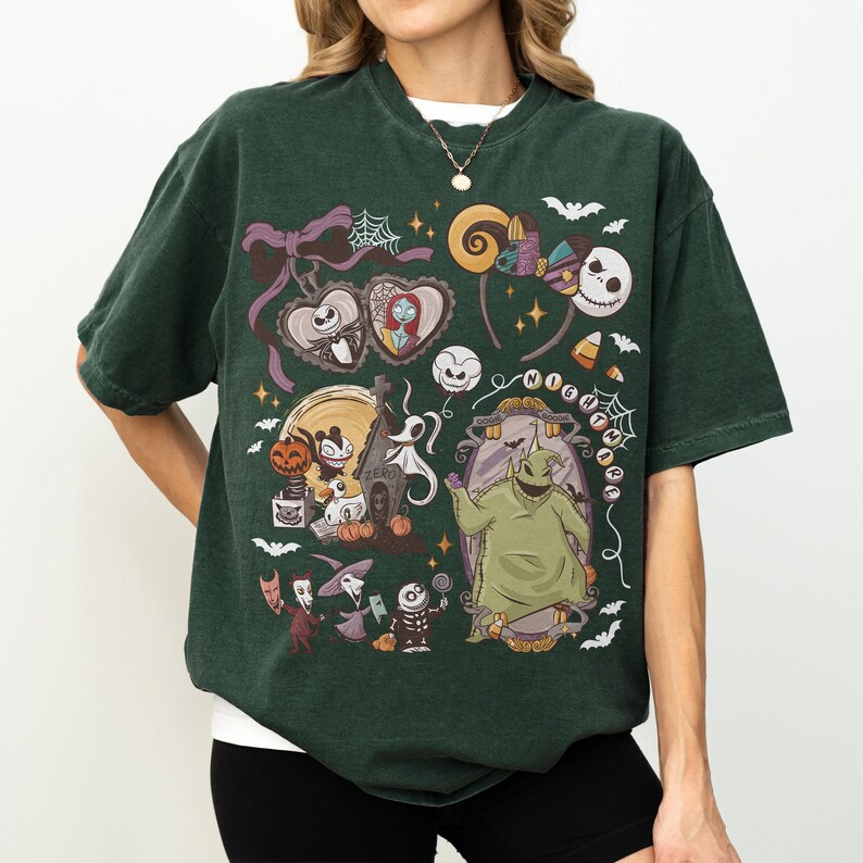 May include: Dark green t-shirt with a colourful graphic design featuring characters from "The Nightmare Before Christmas." The design includes Jack Skellington, Sally, Zero, Oogie Boogie, and other iconic imagery. The shirt has a crew neck and short sleeves.