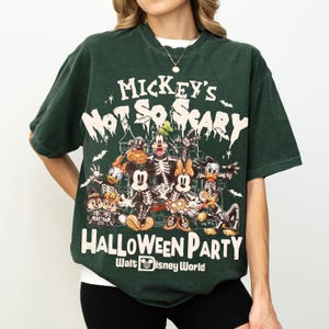 May include: Dark green t-shirt featuring a graphic of Disney characters in skeleton costumes. The text on the shirt reads "Mickey's Not So Scary Halloween Party" and "Halloween Party Walt Disney World". The shirt has short sleeves and a crew neck.