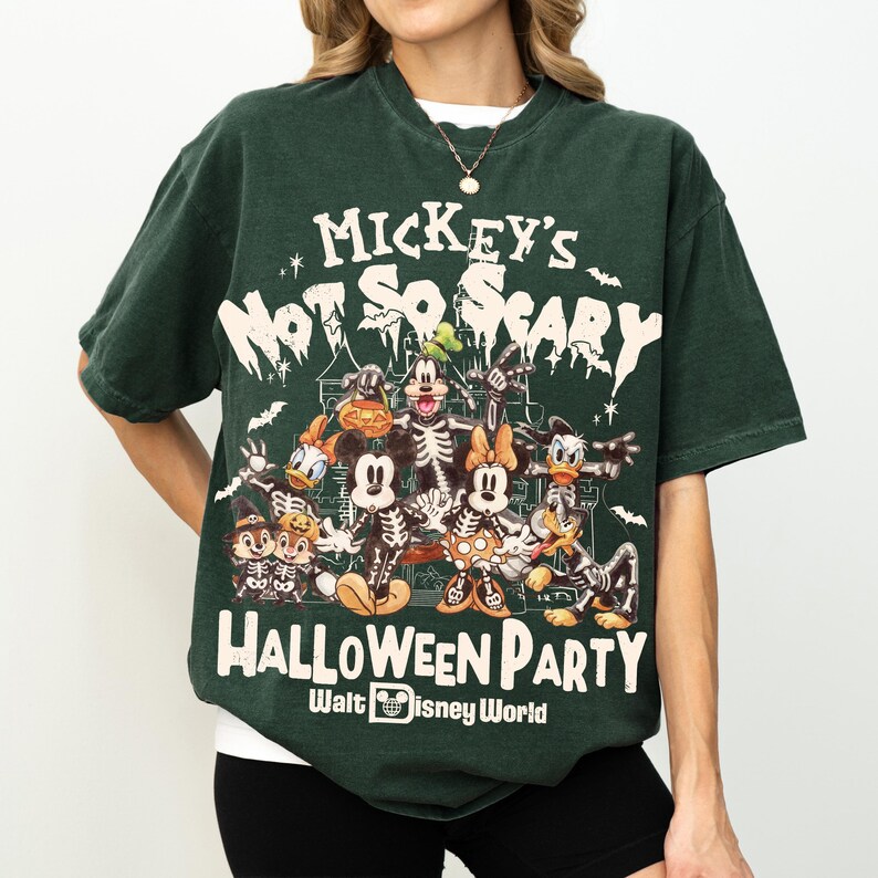 May include: Dark green t-shirt featuring a graphic of Disney characters in skeleton costumes. The text on the shirt reads "Mickey's Not So Scary Halloween Party" and "Halloween Party Walt Disney World". The shirt has short sleeves and a crew neck.