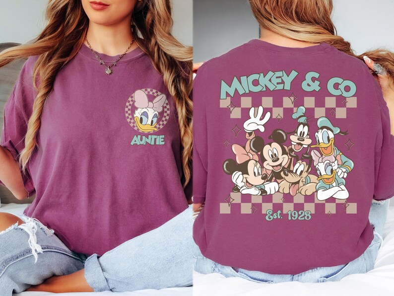 K&ouml;nnte beinhalten: Pflaumenfarbenes T-Shirt mit Daisy Duck und dem Wort "Auntie" sowie einem Mickey & Co.-Design mit Mickey, Minnie, Goofy, Donald und Daisy Duck. Auf der R&uuml;ckseite des Shirts steht "Mickey & Co." und "Est. 1928".
