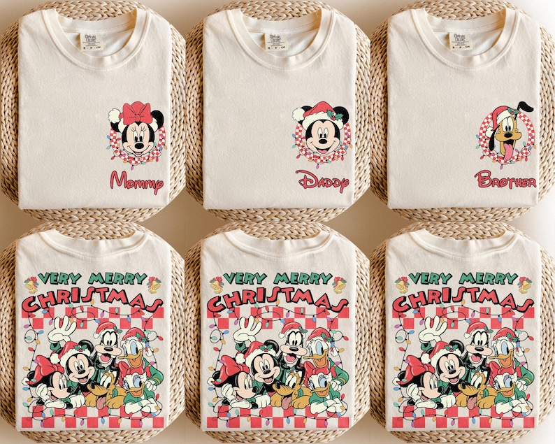 May include: Cream-coloured t-shirts featuring festive graphics. Designs include Minnie Mouse, Mickey Mouse, and Pluto in Santa hats, and a group graphic with the text "VERY MERRY CHRISTMAS". The shirts are displayed on woven mats.