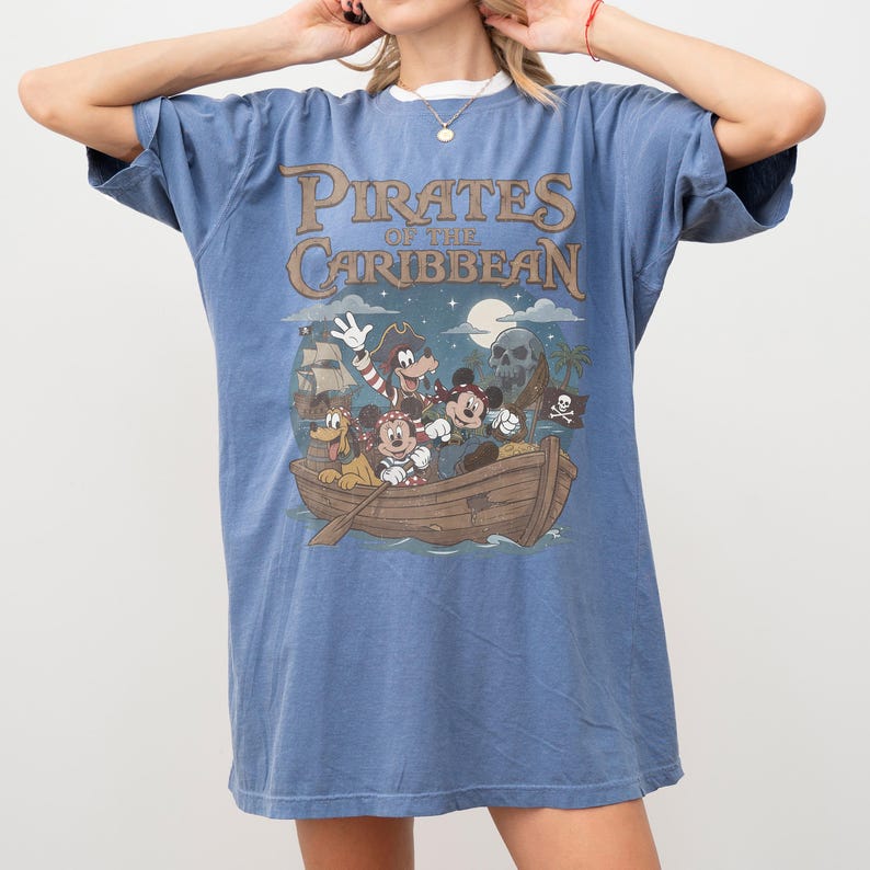 K&ouml;nnte beinhalten: Blaues T-Shirt mit einem "Fluch der Karibik"-Motiv mit Micky Maus und Freunden in einem Boot. Das Shirt hat einen Rundhalsausschnitt und kurze &Auml;rmel.