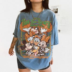 May include: A blue t-shirt featuring a graphic print of Mickey Mouse, Minnie Mouse, Donald Duck, Daisy Duck, Goofy, and Pluto wearing skeleton costumes. The text reads Mickey's Not-So-Scary Halloween Party and Walt Disney World.